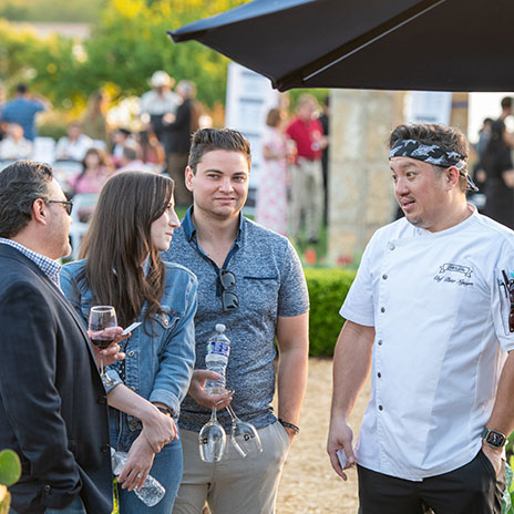 A group of people standing and conversing outdoors with a chef at the Bits and Bites event.