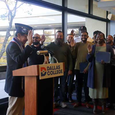 Students gather around a podium and raise their hand in agreement with the speaker