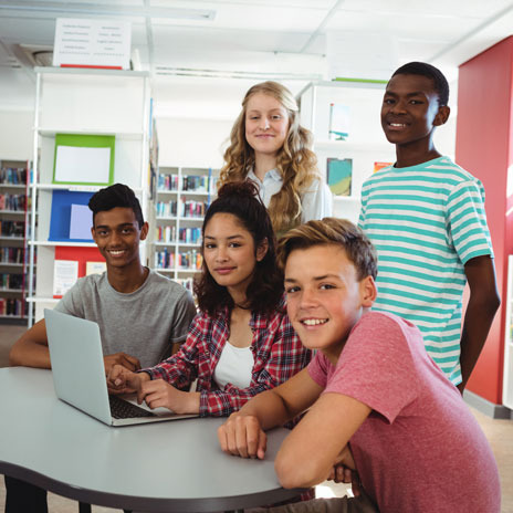 Five students collaborating around a laptop in a library setting