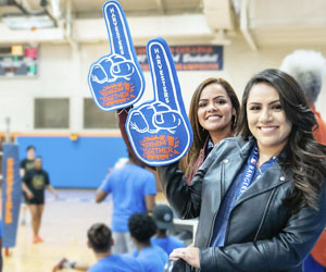 Fans of Eastfield athletics hold up large foam hands with the #1 sign at a volleyball game