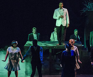 Eastfield students perform a theater production on a dark stage with a green light falling on the cast