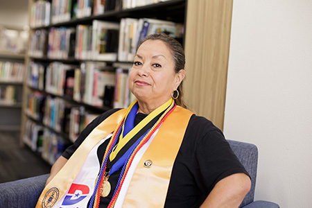 Marisol Perez sits in the library wearing her graduation regalia.