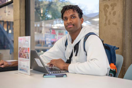 A student sits at a table with a laptop