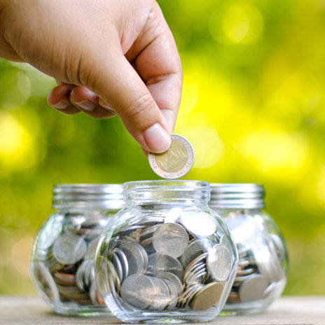 a persons hand putting coins inside a jar to save