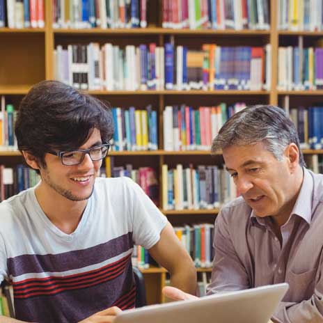 Two people looking at a laptop together, with bookshelves in a library.