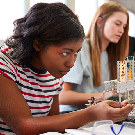 Two individuals working on a small mechanical structure with gears and rods