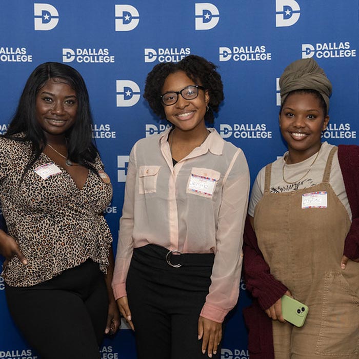 Three members of the Women's Empowerment Network pose for a photo in front a Dallas College backdrop