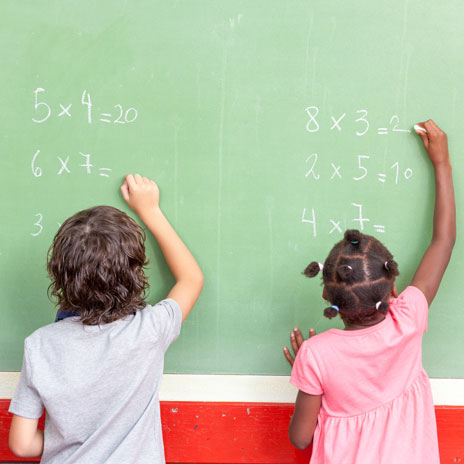 Two students write math problems on a chalkboard.