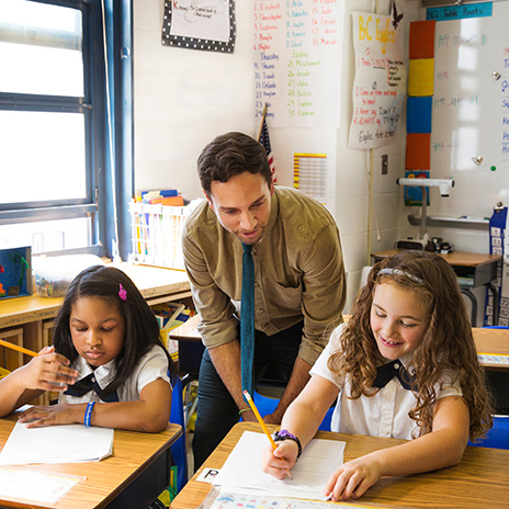 A teacher looks over a students shoulder as she writes notes at her desk