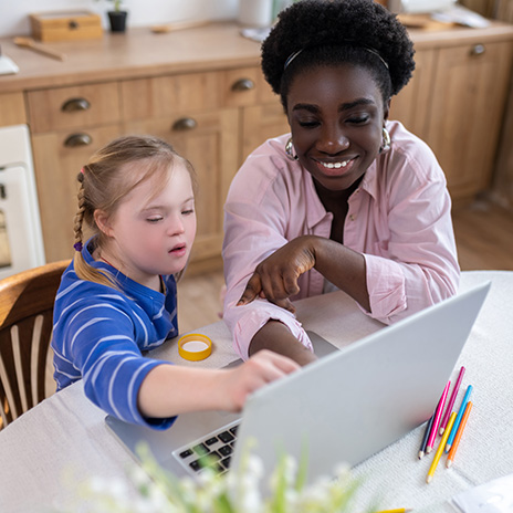 A student and a young student sit at a table and point to a laptop screen