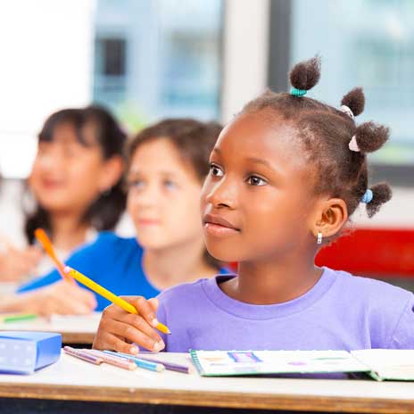 Students sit at their desk with pencils out, listening to their teacher.