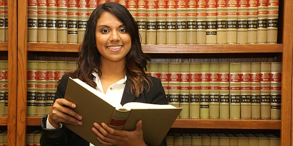 A woman stands in a law library, holding an open book