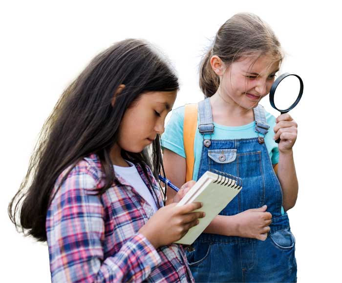 Two girls at youth camp engaged in an outdoor activity. One holds a notebook and pen, concentrating on writing, while the other inspects with a magnifying glass