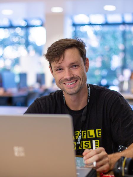 A student sits at a desk in the El Centro library, looking up from his laptop.