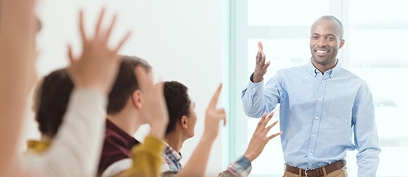 A teacher motions for their adult students to raise their hand